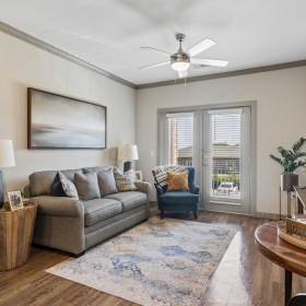 Model living room at Alders Rockwall Active Adult Apartments in Rockwall, TX, featuring wood grain floor paneling.