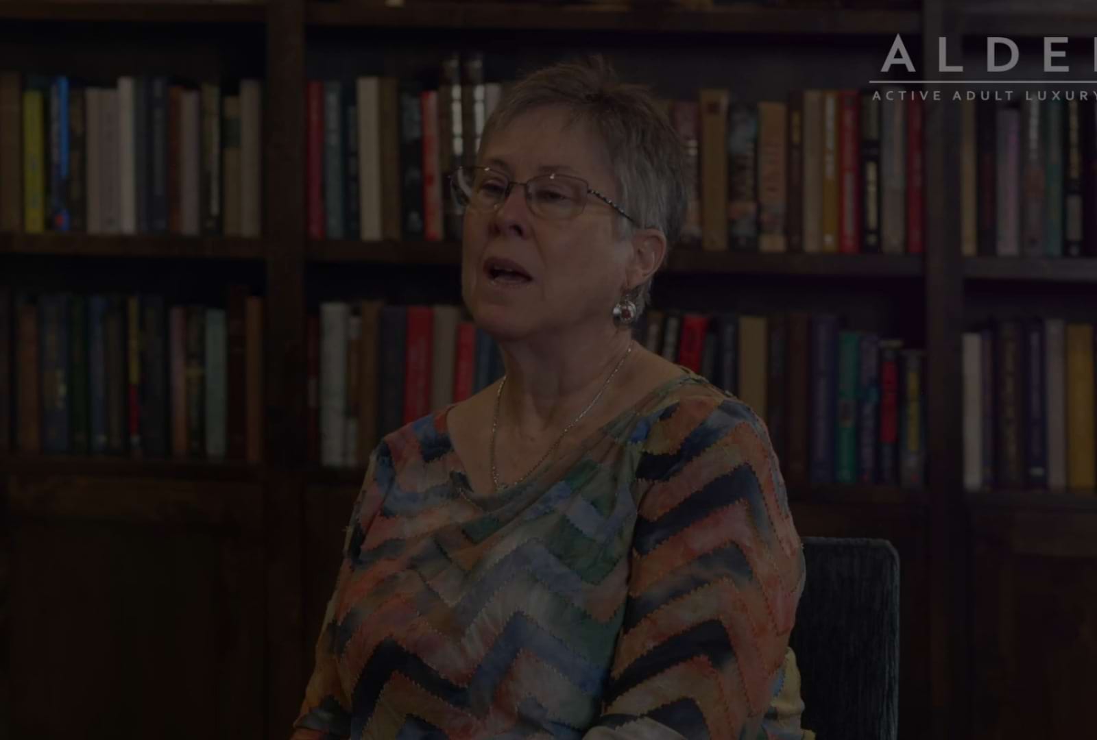 A resident sitting in the lounge at Alders Rockwall Active Adult Apartments in Rockwall, TX, featuring book shelves.